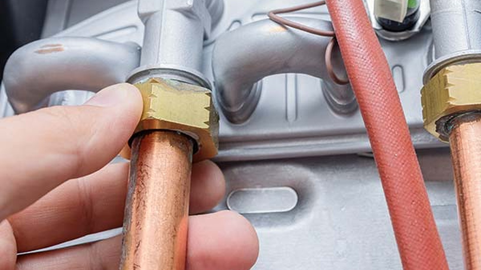 Close-up of a technician adjusting brass fittings and copper supply lines on a residential water heater, illustrating the repair-versus-replacement decision for Leesburg, VA homes