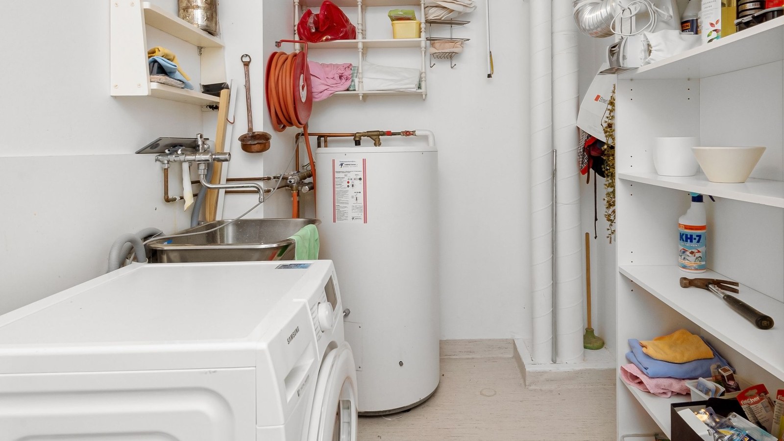 Water Heater Replacement Leesburg Va Complete 2026 Homeowner Guide Floor-standing tank water heater with copper supply connections beside a utility sink and washing machine in a residential utility room, illustrating water heater replacement planning for Leesburg, VA homes